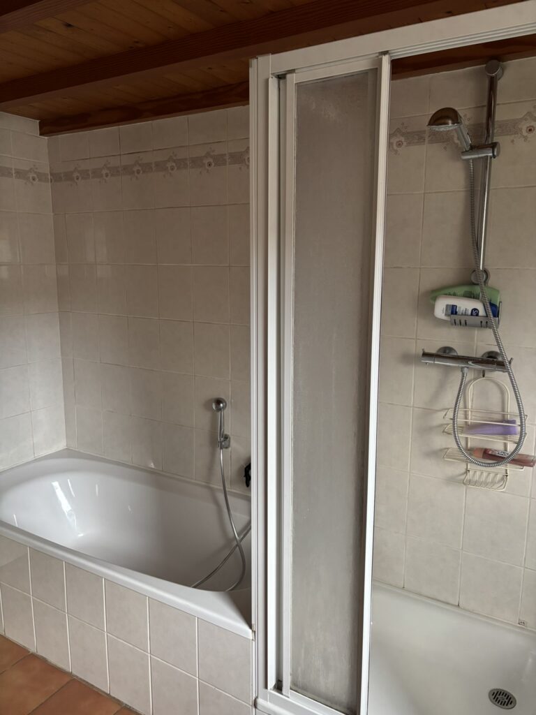 Oude badkamer met ingebouwd bad en douchecabine voor renovatie